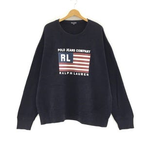 May include: A navy blue sweatshirt with a white and red American flag graphic and the text "Polo Jeans Company" and "Ralph Lauren" printed on the front.