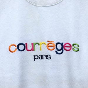 May include: White sweatshirt featuring the embroidered text "courr&egrave;ges paris". The brand name is in a rainbow of colours, with the city name in a smaller, dark blue font. A classic, casual garment.