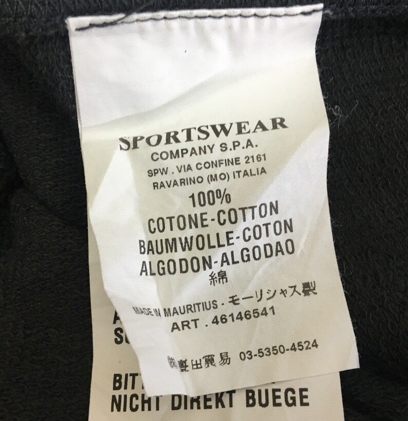 May include: A white clothing tag with black text, featuring the brand name "SPORTSWEAR" and details about the company's location in Italy. The tag also lists the fabric composition as 100% cotton and includes care instructions.