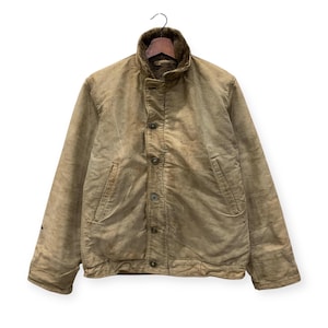May include: A vintage tan jacket with a button-up front and a soft, textured collar. The jacket has two front pockets and a worn appearance, suggesting it has been well-used. The jacket is hanging on a hanger against a white background.