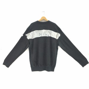 May include: Black sweatshirt with long sleeves, featuring a distressed gray horizontal stripe across the back with the text "STONE ISLAND DENIMS". The sweatshirt is displayed on a wooden hanger against a white background.