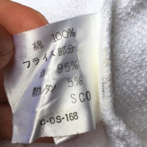 May include: A close-up of a white fabric label with Japanese text and percentages. The label states "100% cotton" and "95%" with other text and numbers. The label is attached to a white garment.