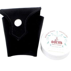 Pode incluir: Uma lata branca de snus Oden's Extreme White portion com uma bolsa de couro preto. A lata tem o texto "Oden's Extreme White Portion Dry" e "Made in Sweden" impresso nela.