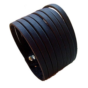 Könnte beinhalten: Schwarzes Lederarmband mit mehreren Lagen Leder, die um das Handgelenk gewickelt sind. Das Armband hat einen silbernen Metallverschluss.