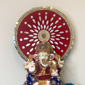 May include: A red and gold Hindu deity statue of Ganesha, the elephant-headed god of wisdom and prosperity. The statue is adorned with jewels and sits on a throne with a decorative circular canopy.