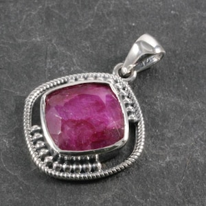 Puede incluir: Un colgante de plata con una piedra preciosa de rubí rosa engastada en un marco cuadrado con un borde de cuentas.