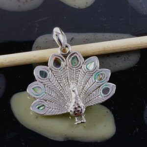 Op de afbeelding: Zilveren pauwenhanger met iriserende groene en blauwe abalone schelp inlegwerk. De staartveren van de pauw zijn waaiervormig uitgespreid.