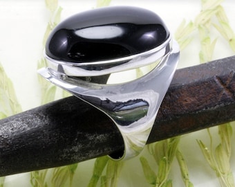 Op de afbeelding: Een zilveren ring met een zwarte ovale edelsteen. De ring heeft een uniek, modern ontwerp met een gebogen band.