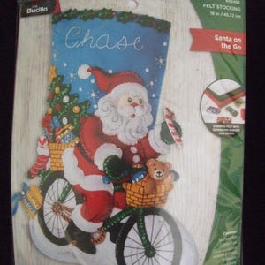May include: Felt Christmas stocking kit featuring Santa Claus riding a bicycle. The stocking is blue with the name "Chase" and a design of Santa, a Christmas tree, and a teddy bear. The kit includes stamped felt, sequins, and beads. The stocking is 18 inches (45.72 cm) long.