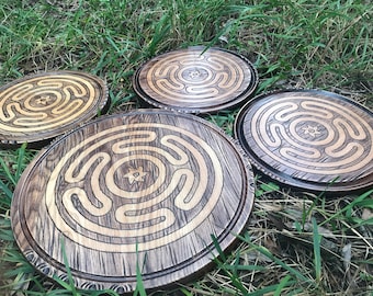 May include: Four wooden circular trays with a carved labyrinth design in the center. The trays are dark brown with a light brown labyrinth design. The trays are arranged in a circle on a bed of green grass.