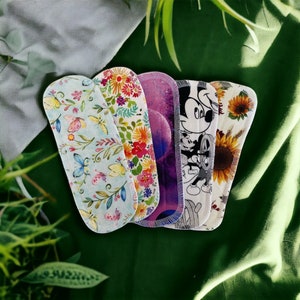 May include: Five reusable cloth pads with various colourful patterns. The pads feature floral designs, butterflies, and a cartoon character.