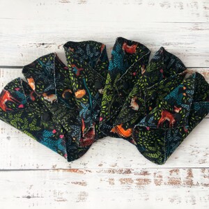 May include: A collection of reusable cloth menstrual pads. Each pad features a black background with a forest-themed pattern of foxes, leaves, and other foliage in shades of orange, green, and teal. The pads are folded and secured with black snaps.
