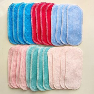 K&ouml;nnte beinhalten: Eine Ansammlung farbenfroher, rechteckiger Stoffeinlagen in Blau-, Rot-, Hellblau-, Rosa- und T&uuml;rkist&ouml;nen. Die Einlagen sind in Reihen angeordnet und zeigen ihre weiche Textur und gen&auml;hten Kanten. Diese wiederverwendbaren Einlagen sind f&uuml;r Stoffwindeln.