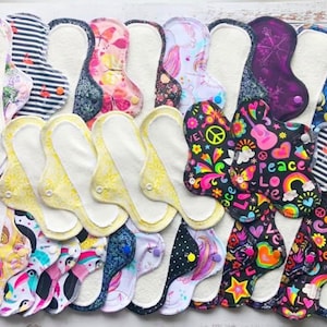 May include: A collection of reusable cloth menstrual pads with various colorful patterns, including floral, geometric, and abstract designs. Some pads feature text like "Peace" and "Love".