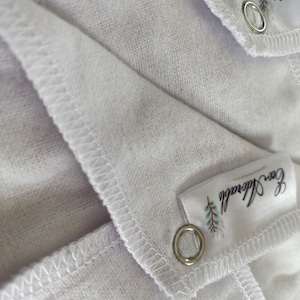 May include: Two white cotton muslin cloths with a stitched edge and a silver grommet. Each cloth has a white label with the text "Eco friendly" and a small green leaf design.