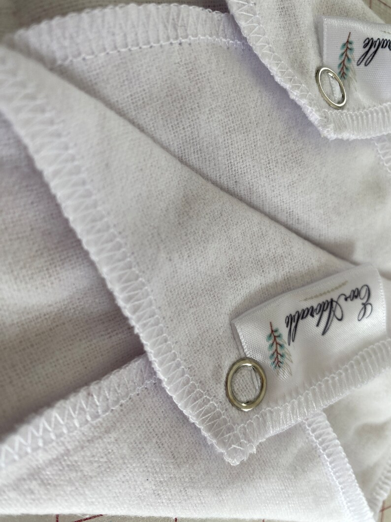 May include: Two white cotton muslin cloths with a stitched edge and a silver grommet. Each cloth has a white label with the text "Eco friendly" and a small green leaf design.