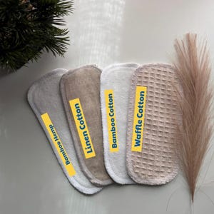 May include: Four oval-shaped fabric pads arranged in a row, labeled with yellow strips reading Bamboo Hemp, Linen Cotton, Bamboo Cotton, and Waffle Cotton. The pads feature distinct textures including smooth, woven, and waffle-knit surfaces in neutral tones.
