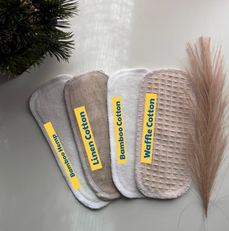 May include: Four oval-shaped fabric pads arranged in a row, labeled with yellow strips reading Bamboo Hemp, Linen Cotton, Bamboo Cotton, and Waffle Cotton. The pads feature distinct textures including smooth, woven, and waffle-knit surfaces in neutral tones.