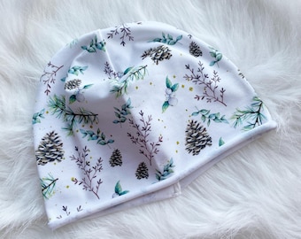 May include: White beanie with a wintery floral pattern featuring pine cones, leaves, and berries. The beanie has a folded cuff.