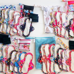 May include: A collection of reusable cloth menstrual pads in various colors and patterns, with matching storage bags. The pads are arranged in stacks and are ready to be used.