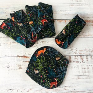 May include: Reusable cloth menstrual pads with a forest animal print. The pads feature a black background with foxes, deer, rabbits, and other forest creatures. The pads are in various shapes and sizes, with snaps for secure closure.