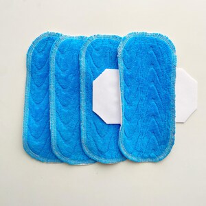 K&ouml;nnte beinhalten: Vier blaue Mikrofaser-Wischmopp-Pads mit strukturiertem Muster und wei&szlig;er Umrandung. Ein wei&szlig;es, sechseckiges Pad befindet sich zwischen zwei der blauen Pads. Die Pads sind zum Reinigen bestimmt.
