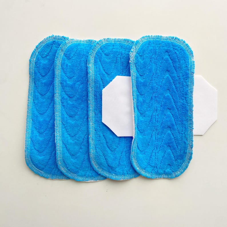 K&ouml;nnte beinhalten: Vier blaue Mikrofaser-Wischmopp-Pads mit strukturiertem Muster und wei&szlig;er Umrandung. Ein wei&szlig;es, sechseckiges Pad befindet sich zwischen zwei der blauen Pads. Die Pads sind zum Reinigen bestimmt.