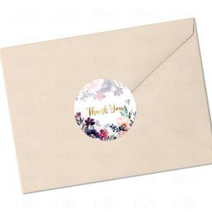 May include: A round, white sticker with a floral design in shades of purple, pink, and blue. The sticker has the words "Thank You" written in gold lettering.