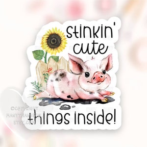 May include: A watercolor illustration of a pink piglet with black spots laying in mud. The piglet is looking at the viewer with a happy expression. A sunflower is growing in the background. The text "Stinkin' cute things inside!" is written on the sticker.