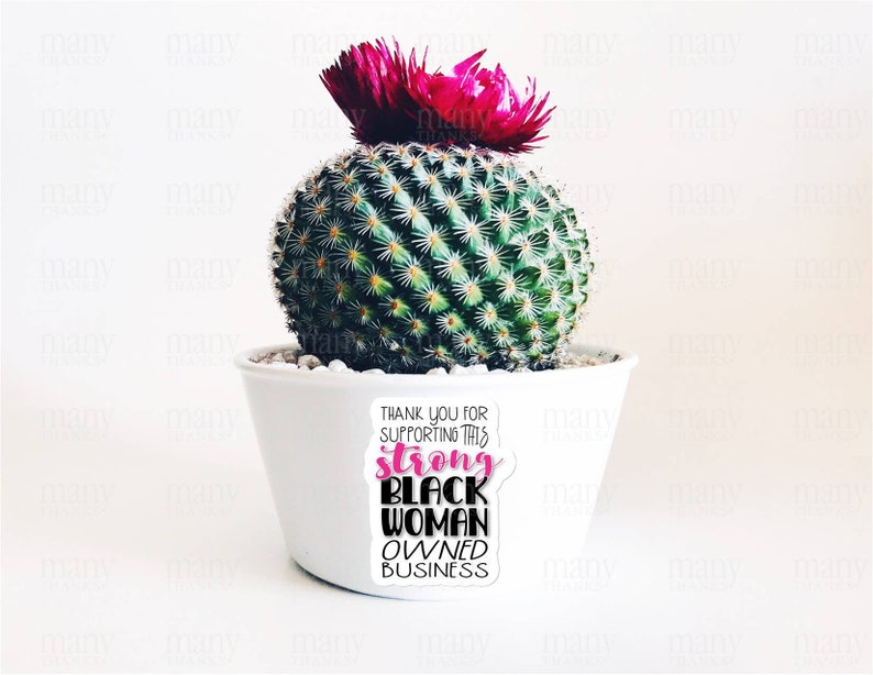 May include: A white ceramic pot with a cactus plant and a pink flower on top. The pot has a sticker that says "Thank you for supporting this strong black woman owned business".