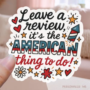 Op de afbeelding: Een witte sticker met de tekst "Leave a review, it's the AMERICAN thing to do!" in zwart, rood en blauw. Het woord "AMERICAN" is ontworpen met de Amerikaanse vlag. De sticker heeft sterren, harten en een vuurwerk.