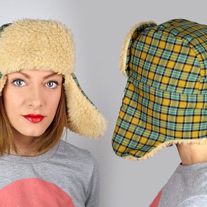 May include: A yellow, green, and black plaid trapper hat with a cream-colored faux fur brim and ear flaps.