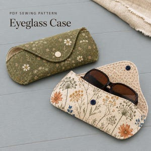 Puede incluir: Dos estuches de tela para gafas con estampados florales. Uno es verde oliva con flores blancas y cierre a presión. El otro es crema con flores silvestres naranjas y azules, contiene gafas de sol oscuras y tiene un cierre a presión azul. Texto: PDF SEWING PATTERN Eyeglass Case.