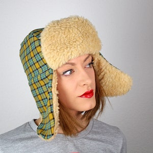 May include: A yellow and green plaid trapper hat with a white faux fur brim and ear flaps.