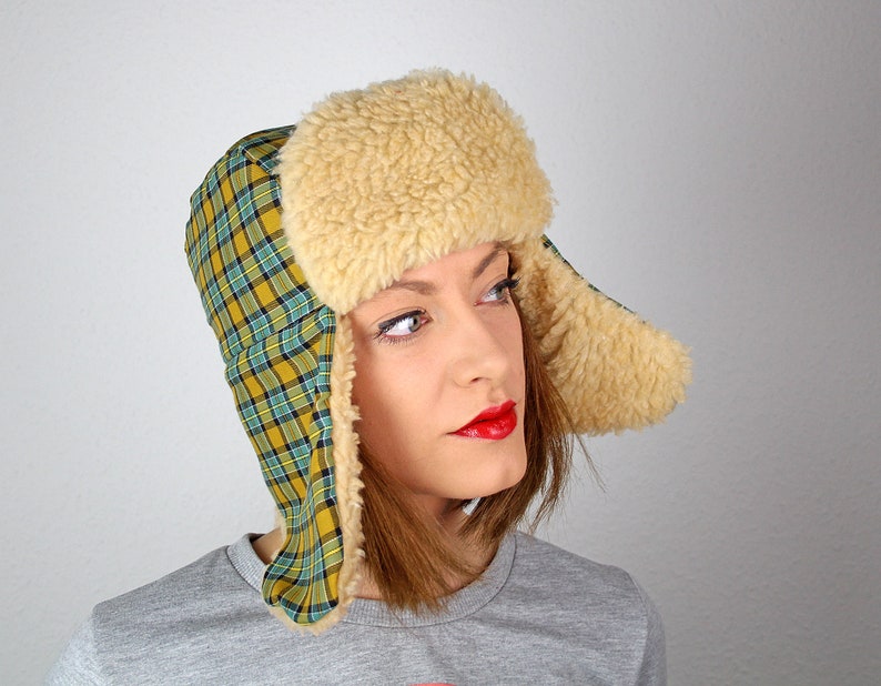 May include: A yellow and green plaid trapper hat with a white faux fur brim and ear flaps.