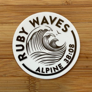 May include: White round sticker with black text and a black and white wave design. The text reads "RUBY WAVES ALPINE 38:08".