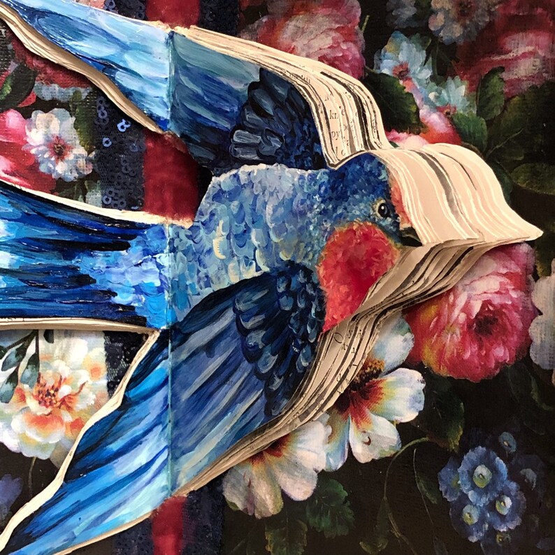 May include: A bluebird painted on a stack of pages with a floral background. The bird has a red breast and blue wings. The pages are open and the bird is perched on the top of the stack.