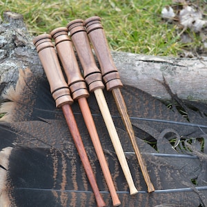 以下が含まれることがあります： 明るい茶色から濃い茶色まで、さまざまな木の色合いの木製ゲームコールが4つ、七面鳥の羽と風化した丸太の上に置かれています。 コールは、フレアトップと細いテーパーベースを備えた円筒形のデザインです。