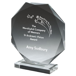 May include: A clear, faceted glass award with a rectangular base. The award features the text "The Worshipful Company of Weavers St Andrew's Vision Award" and "Amy Sudbury". The top of the award has the text "Reaching for the stars".