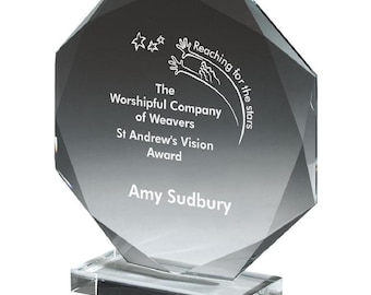 Może przedstawiać: Przezroczysta, fasetowana szklana nagroda z prostokątną podstawą. Nagroda zawiera tekst "The Worshipful Company of Weavers St Andrew's Vision Award" i "Amy Sudbury". Na górze nagrody znajduje się napis "Reaching for the stars".