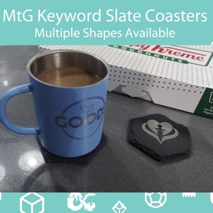 May include: Slate coasters with the text "MtG Keyword Slate Coasters" and "Multiple Shapes Available". A blue mug with the text "THE GOOD" sits on a coaster. A box of donuts is in the background.