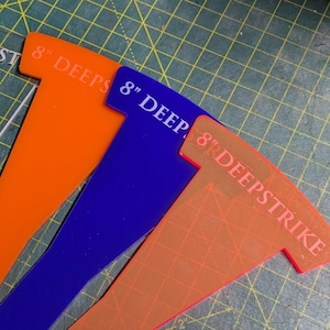 May include: Three plastic T-shaped tools in orange, blue, and reddish-orange. Each tool has the text "8" DEEPS" or "8" DEEPSTRIKE" printed on it. The tools are on a green cutting mat.