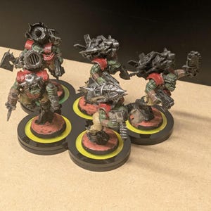 Peut inclure: Cinq figurines miniatures d'orcs &agrave; la peau verte, v&ecirc;tus d'une armure rouge et arm&eacute;s d'armes m&eacute;talliques. Ils sont plac&eacute;s sur des socles circulaires avec des accents jaunes et rouges, dispos&eacute;s sur une plateforme noire multi-socles. Les orcs sont d&eacute;taill&eacute;s avec diverses armes et &eacute;quipements.