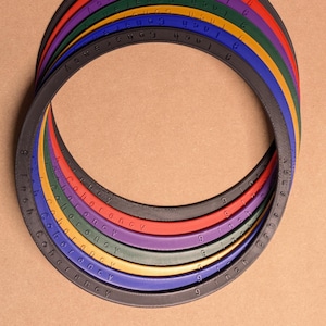 Peut inclure: Une collection d'anneaux circulaires de différentes couleurs, notamment noir, bleu, jaune, vert, violet et rouge. Chaque anneau présente le texte en relief "Coherency" et "9 inch" sur sa surface, disposés en un motif circulaire superposé.