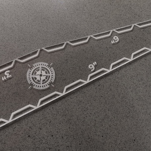 May include: Clear acrylic quilting ruler with a compass rose design and measurements in inches. The ruler is approximately 9 inches (22.86 cm) long and features angled edges and etched markings for precise cutting and alignment.