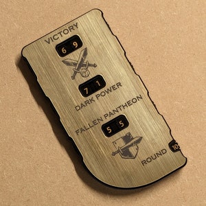Puede incluir: Un contador de juego rectangular de color dorado con texto y números negros. El contador presenta las palabras "VICTORY", "DARK POWER", "FALLEN PANTHEON" y "ROUND". También tiene ilustraciones de espadas cruzadas, un escudo y un dado.