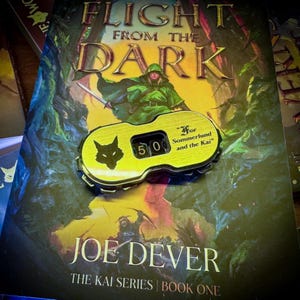 Può includere: Copertina del libro "Flight From The Dark" di Joe Dever, con una figura in verde e una spada. Un contatore giallo con un simbolo di lupo e il numero 50 è sul libro. Il testo "For Sommerlund and the Kai" è anch'esso visibile.