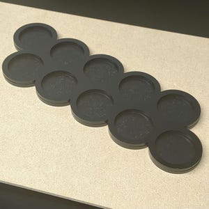 Peut inclure: Un plateau noir avec plusieurs cavit&eacute;s circulaires, con&ccedil;u dans un motif distinctif et connect&eacute;. La couleur sombre et le design simple du plateau cr&eacute;ent une esth&eacute;tique moderne. Les cavit&eacute;s circulaires sont id&eacute;ales pour contenir de petits objets.