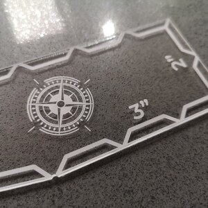 May include: Clear acrylic quilting template with a compass rose design and measurements. The template is 3 inches by 2 inches.