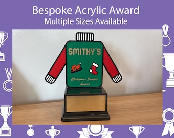 May include: A bespoke acrylic award shaped like a Christmas jumper. The green jumper has red sleeves and features a turkey and stocking graphic. The award sits on a black base with a gold plaque. Text on the award reads "SMITHY'S Christmas Jumper Award".